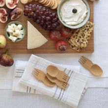 Load image into Gallery viewer, Wooden cutting board with assorted fruits, cheeses, and a bowl of dip on a white surface, with wooden cutlery and a napkin and sporks | Little Twidlets
