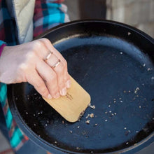 Load image into Gallery viewer, Person cleaning a black pan with a wooden scraper | Little Twidlets
