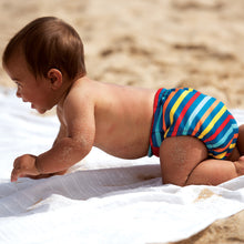 Load image into Gallery viewer, Tots Bots Reusable Swim Nappy Little Twidlets Rainbow stripes on beach 
